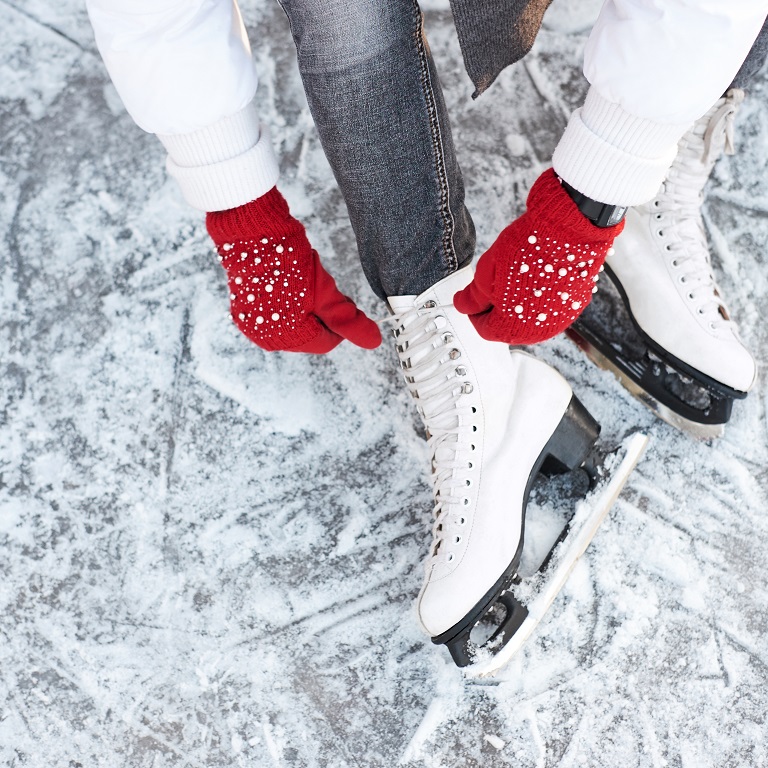 Girl tying shoelaces on ice skates before skating on the ice rink, hands in red knitted gloves. View from top.