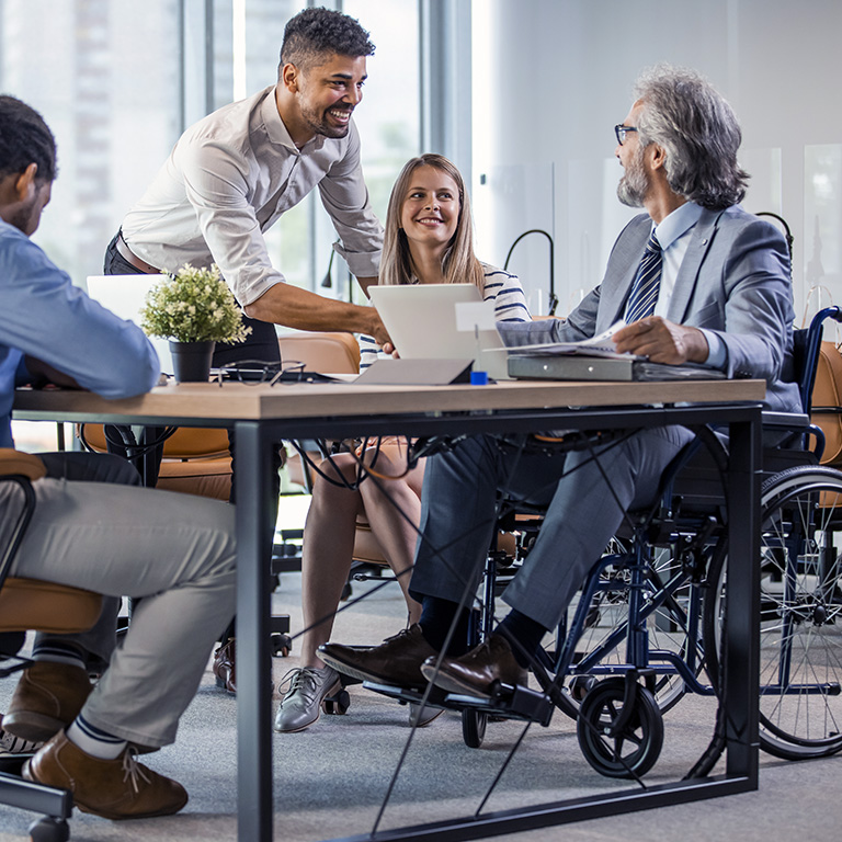 Group of business people in a meeting with colleague in a wheelchair for inclusion. Young businessman greeting handicapped business partner and team. Coworker on wheelchair