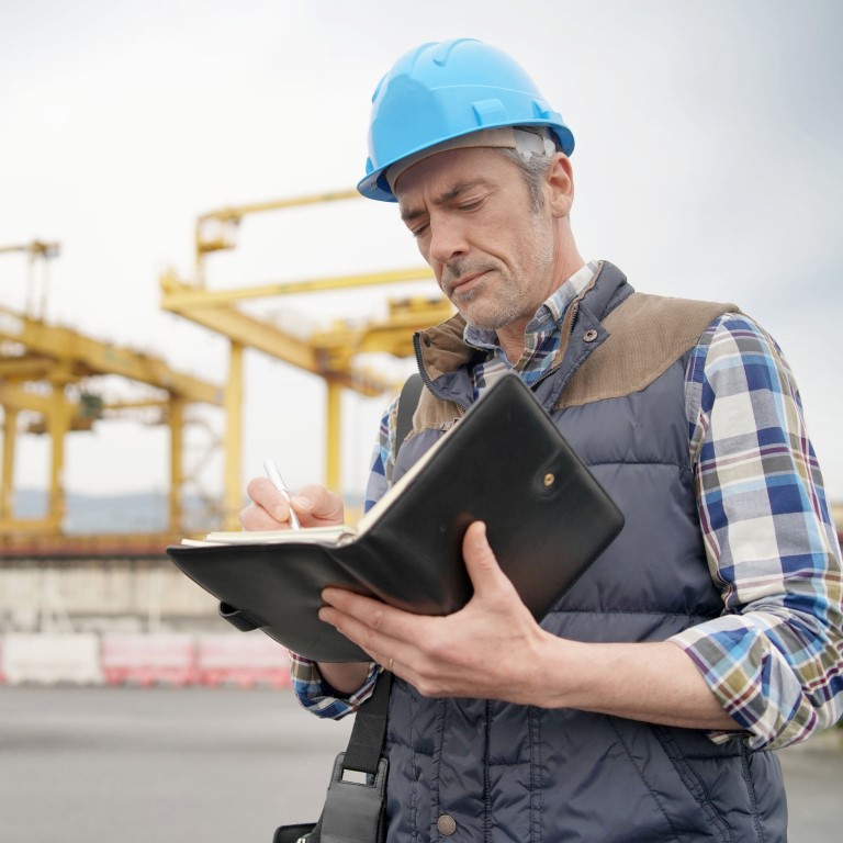 Mature construction worker inspecting worksite with notebook