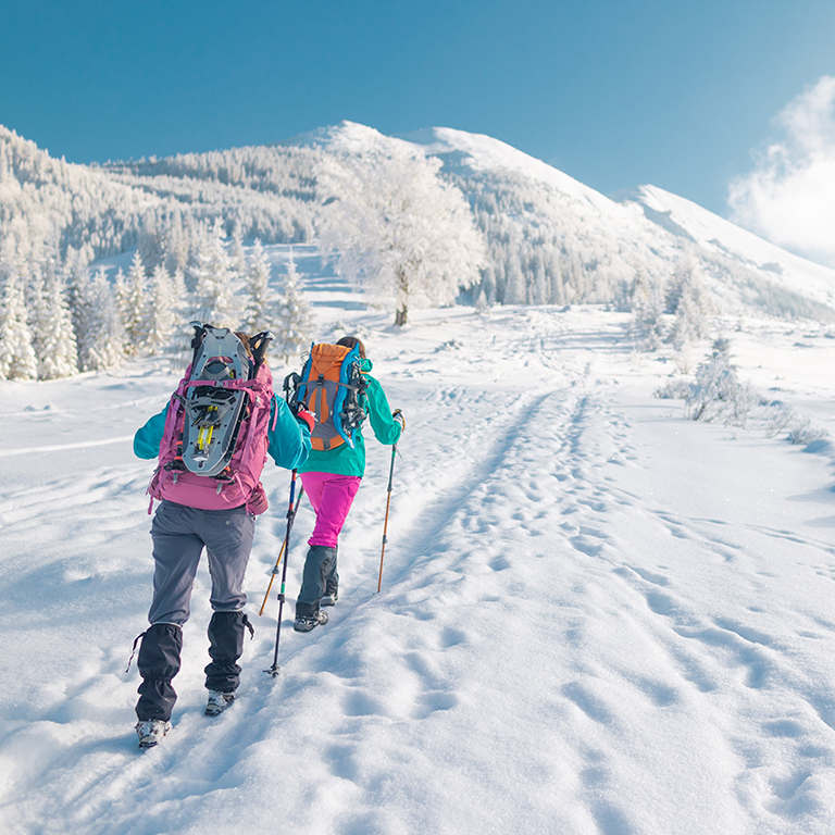 Two women walk with snowshoes on the backpacks, winter trekking, two people in the mountains in winter, hiking equipment