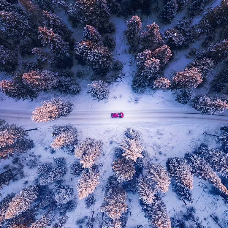 Red car driving on winding road through snowy forest, toning blue. Concept banner winter travel, aerial view.