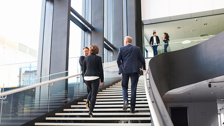 Modern business people walking on stairs in glass hall of office building