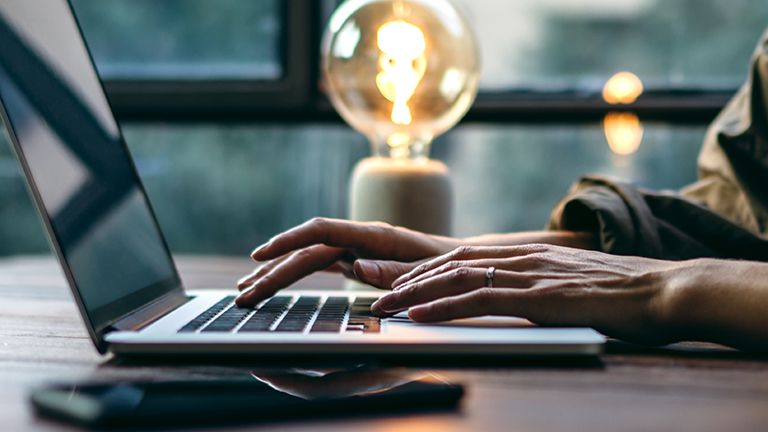 Young woman working with a laptop. Female freelancer connecting to internet via computer. Blogger or journalist writing new article. Close-up of female hands typing on keyboard
