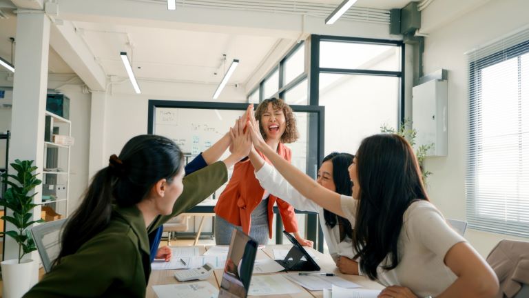 A diverse team of business professionals celebrating with a high-five during an ESG