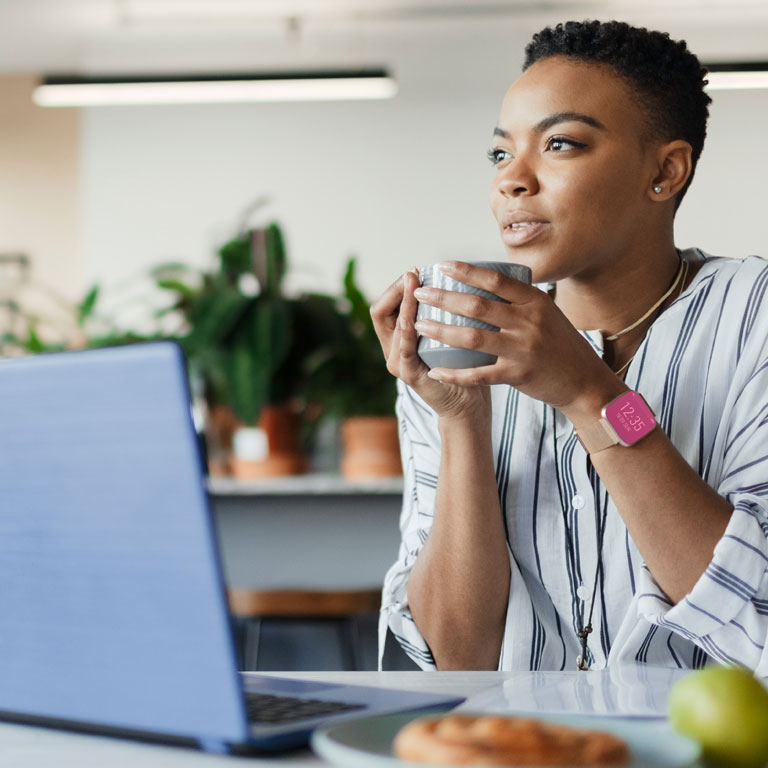 Thoughtful young businesswoman drinking coffee and working at laptop in office lounge