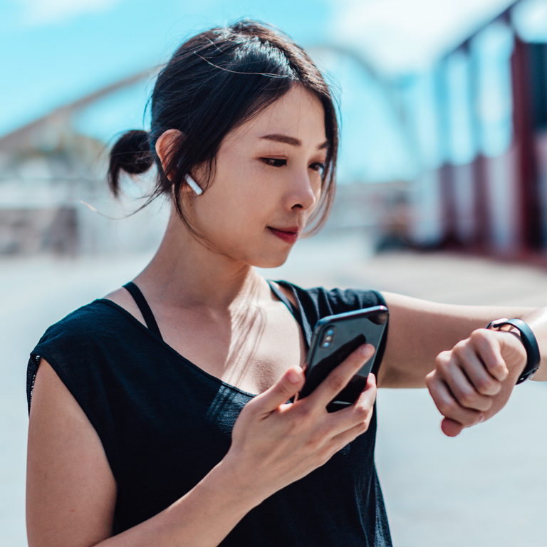 Asian woman looking at watch with smart phone & earpods