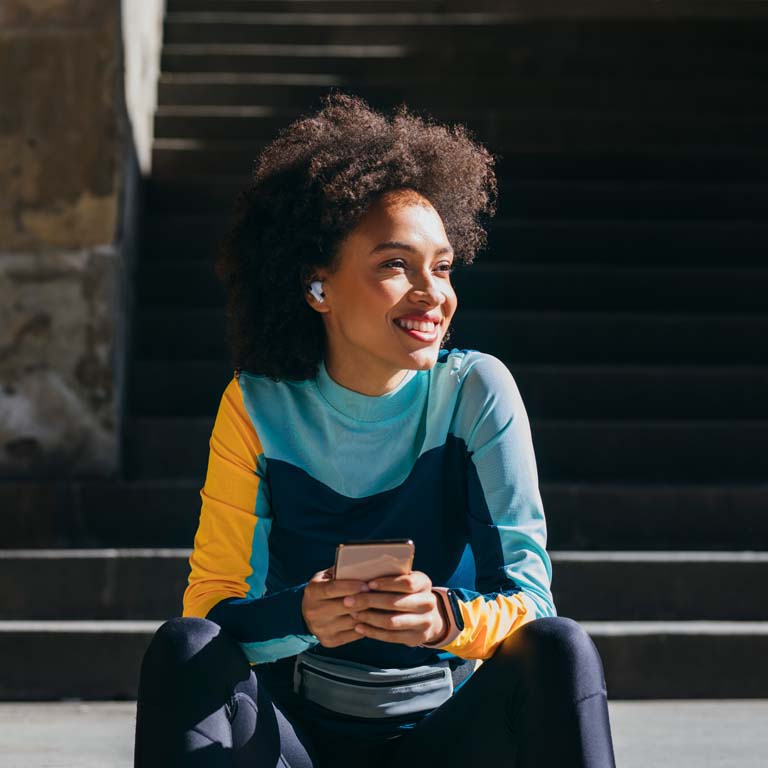 A good-looking young sportswoman sitting on the stairs in the city, taking a break from running.