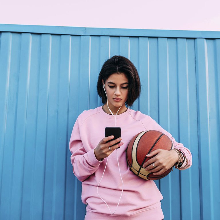 Young woman with basketball, smartphone and earphones