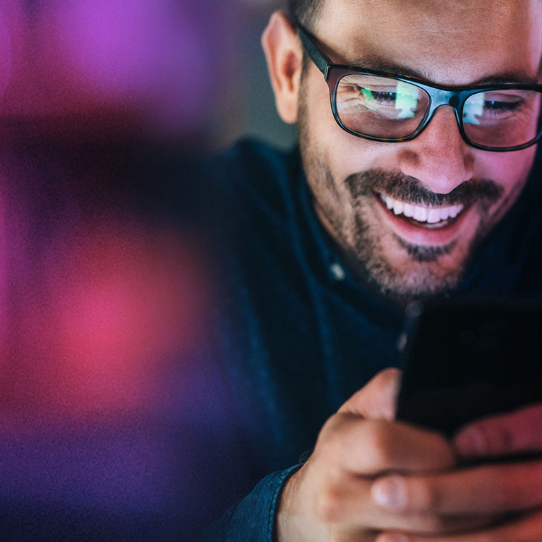Man with glasses smiling at a smartphone