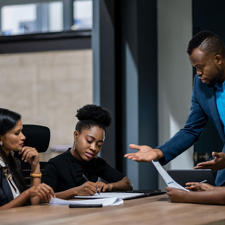 African businessman talking with a diverse group of female colleagues while having a meeting together around a table in an office boardroom