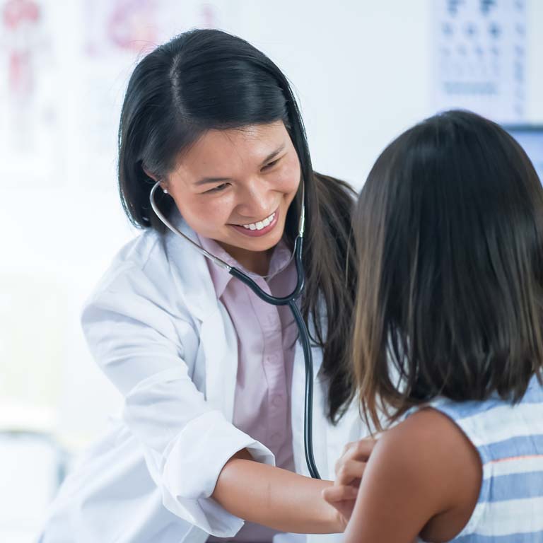 A female doctor of Asian descent is using her stethoscope to listen to her young patient's chest.