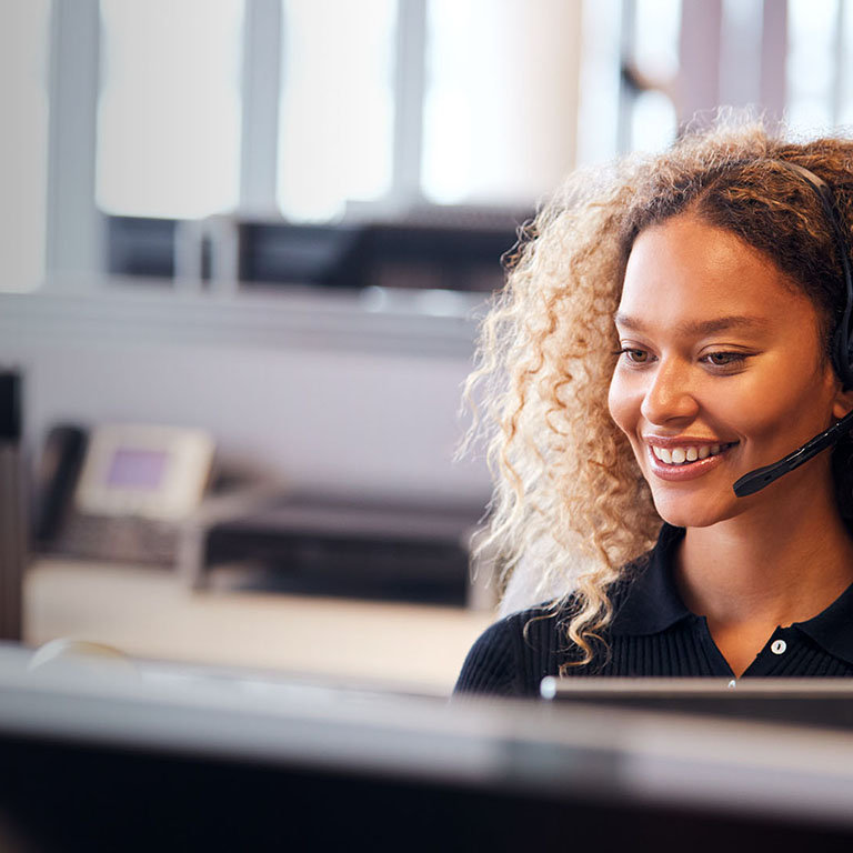 Young Businesswoman Wearing Telephone Headset Talking To Caller In Customer Services Department