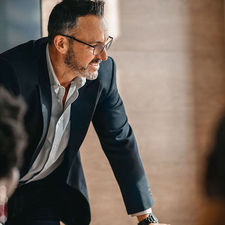 close up of businessman standing over boardroom table in front of South African coworkers during a diverse corporate meeting