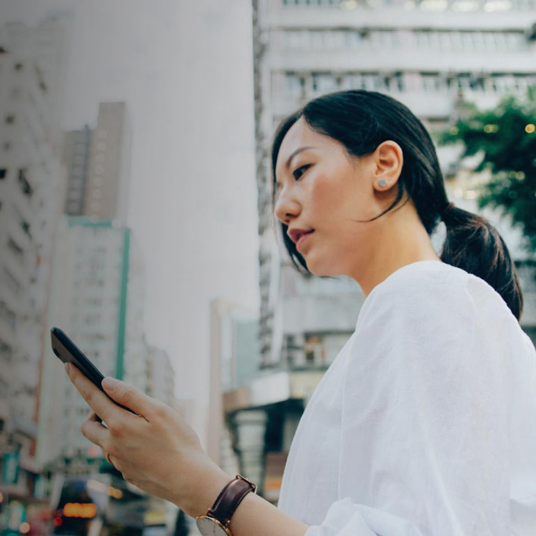 Young East Asian woman in a busy city looking at smartphone