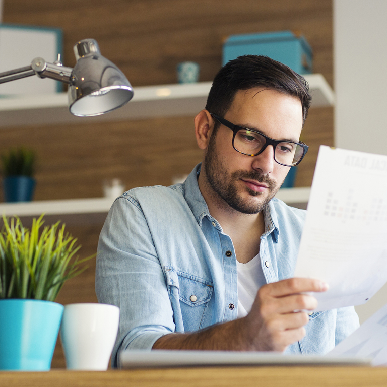 A casually dressed man with beard and glasses looking at document