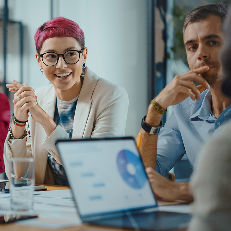 Young millennial with pink hair at boardroom table discussion with older generations