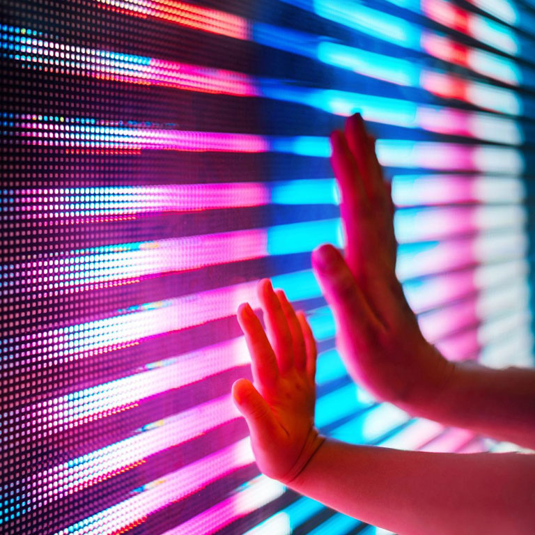 Close up of a mother and child hand touching illuminated and multi-coloured LED display screen, connecting to the future