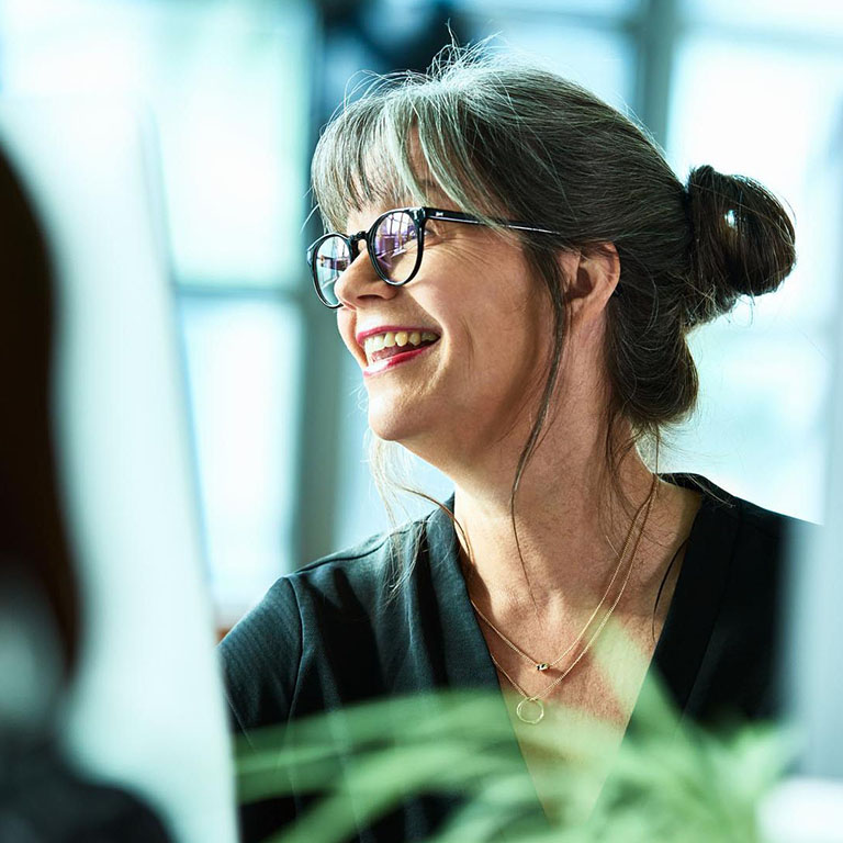 Mature woman with glasses smiling and looking out the window at office