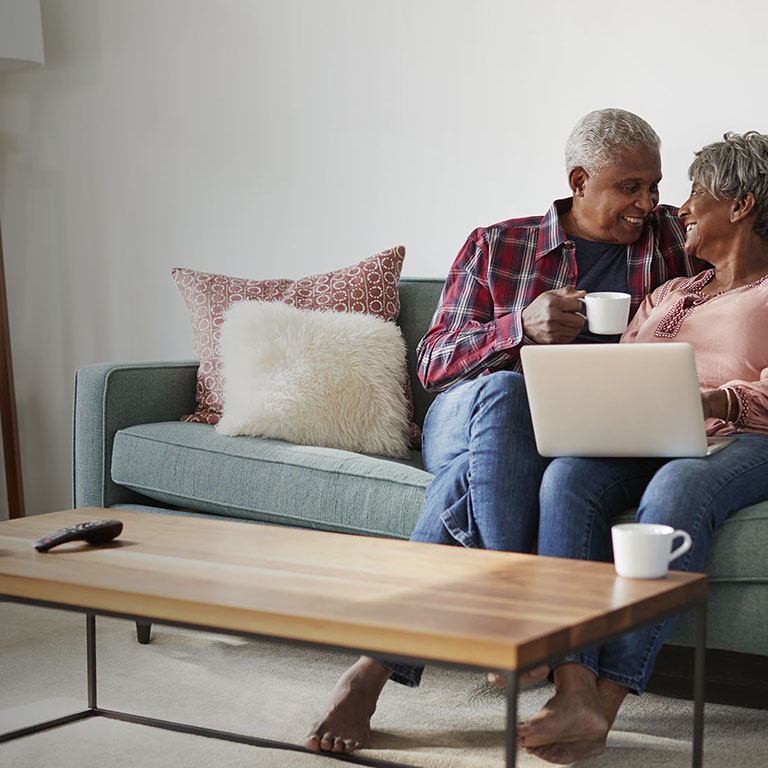 Senior Couple Sitting On Sofa At Home Using Laptop To Shop Online