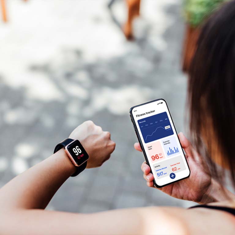 Over the shoulder view of young woman using running app on smart watch and smartphone to track pace and time. Doing exercise with wearable technology. Mockup image for young woman using smartphone and smart watch.