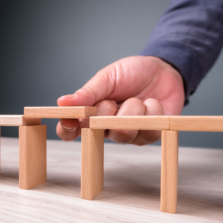 Hand build a toy bridge by wooden blocks and going to add the final piece between the gap to complete, concept of help solution, solve the disconnect problem