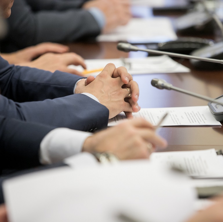 One of politician sitting by table with his hands over document during political summit or conference