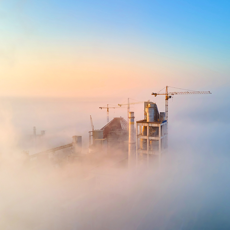 Aerial view of cement factory with high concrete plant structure and tower crane at industrial production site on foggy morning. Manufacture and global industry concept.