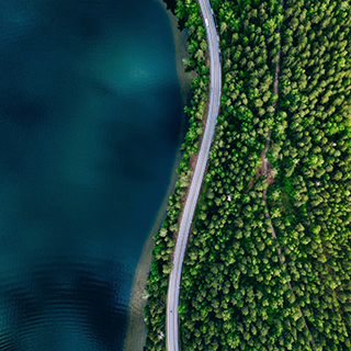 Aerial view of road between green summer forest and blue lake in Finland