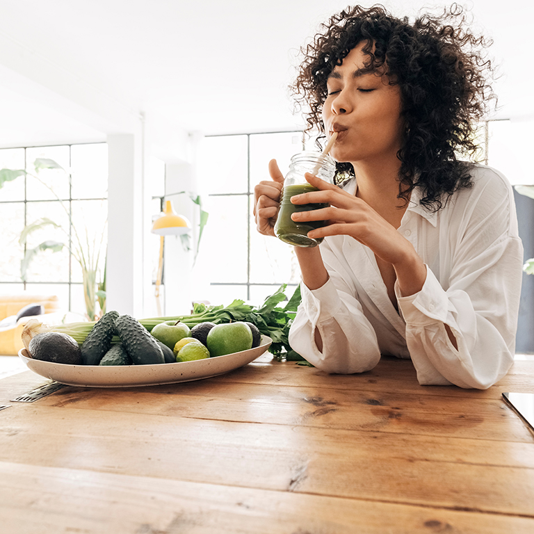 Young african american woman drinking green juice with reusable bamboo straw in loft apartment