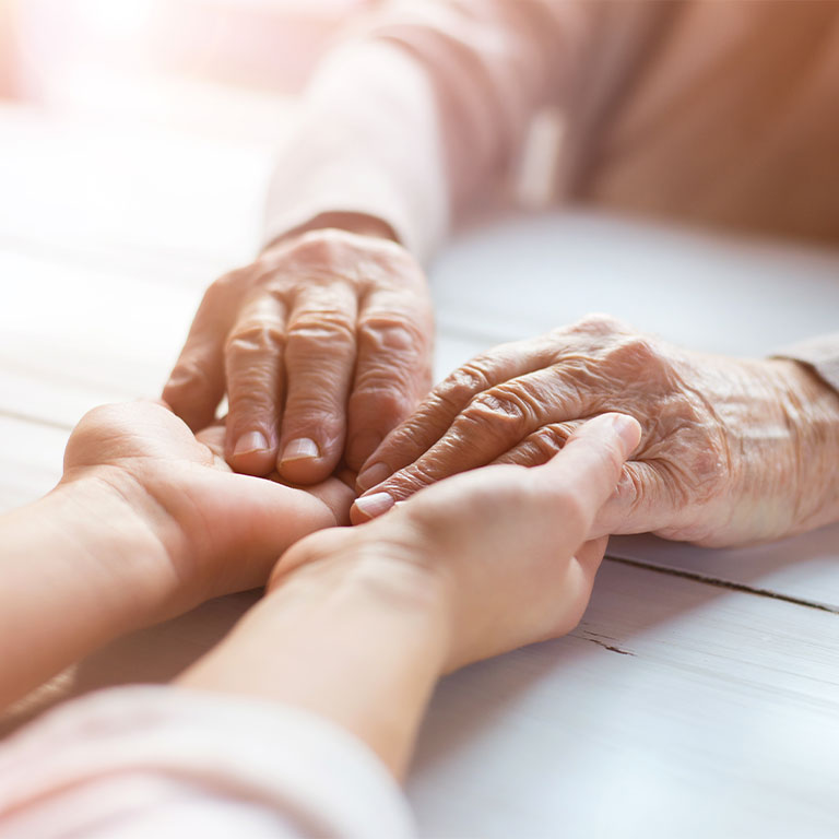 Elderly female holding hand of young caregiver at nursing home.