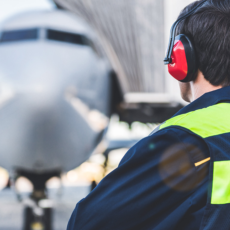 Mechanic working in headset at airport. He looking at plane while turning back to camera