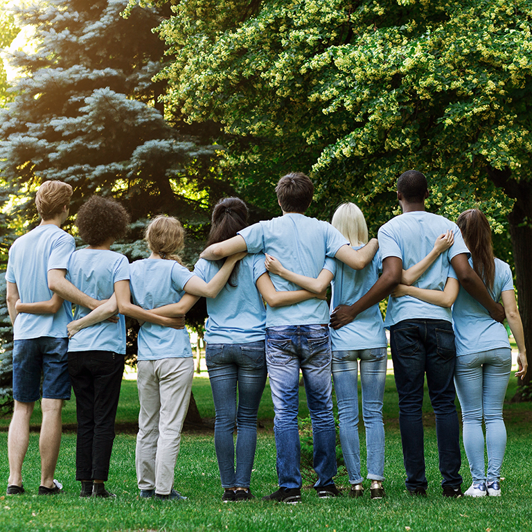 Volunteering, people and ecology concept. Group of volunteers embracing in park, back view, copy space