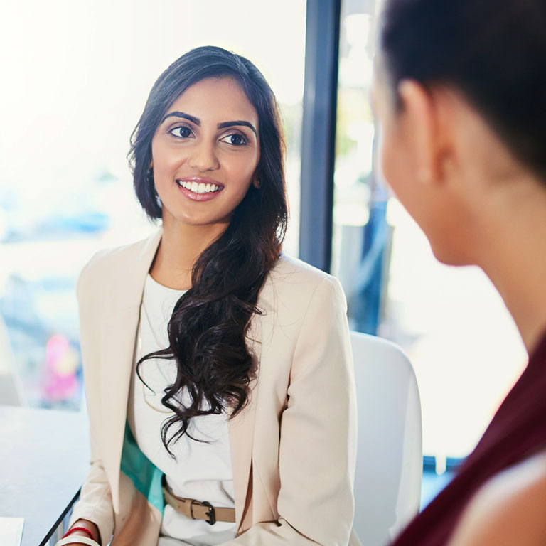 Two young professional business woman talking while sitting in their office