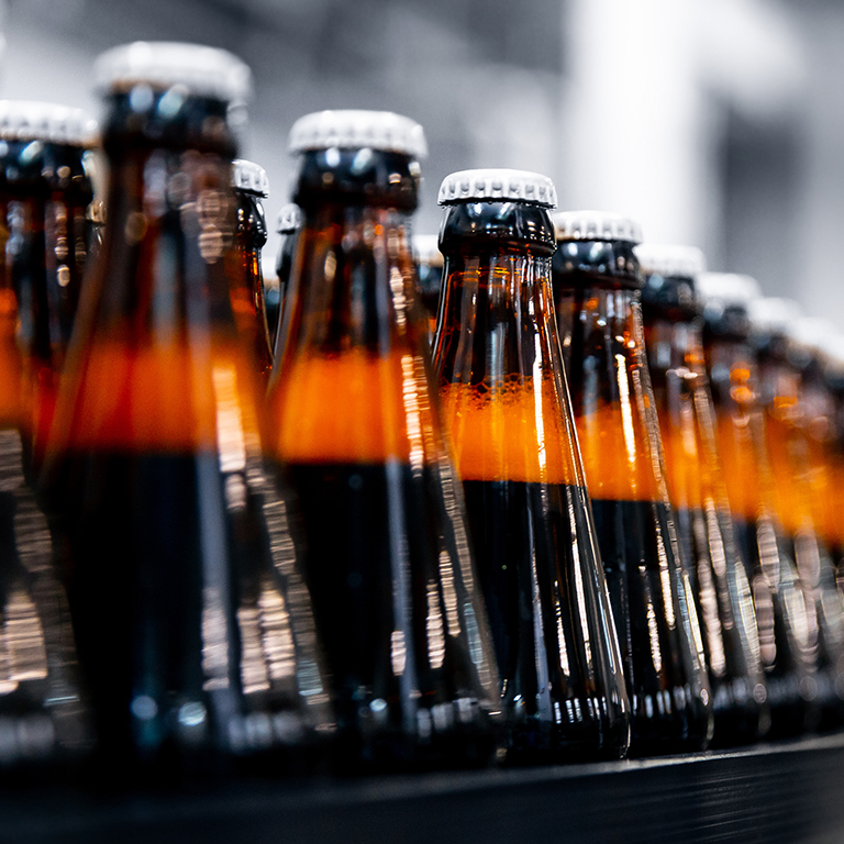 Glass bottles of beverage on dark background with sun light. Concept beverage plant production line.