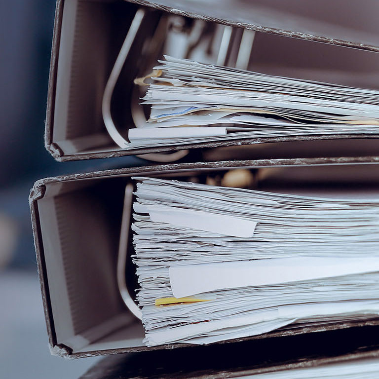 Binders with papers are waiting to be processed by business woman or bookkeeper working at the desk in office back in blur. Audit and tax concept.