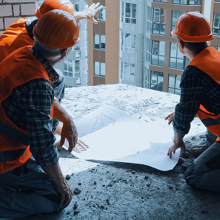 builders in hand hats discussing blueprint while sitting on construction site