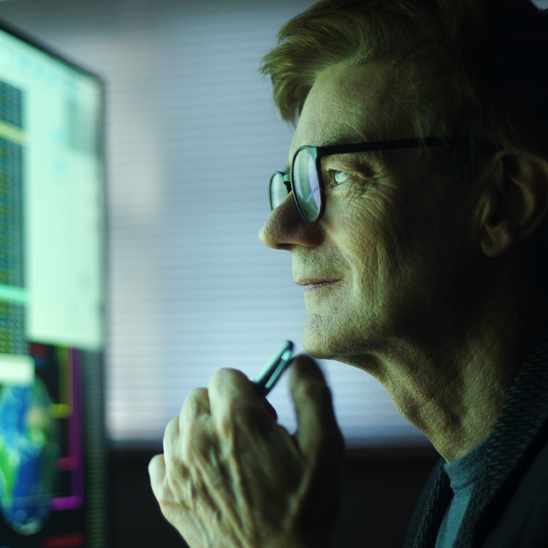 Business man in glasses working in office, staring at computer screen with charts