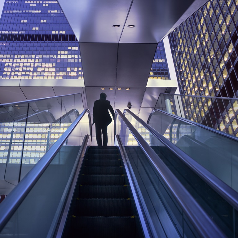 Business person walks up escalator in city