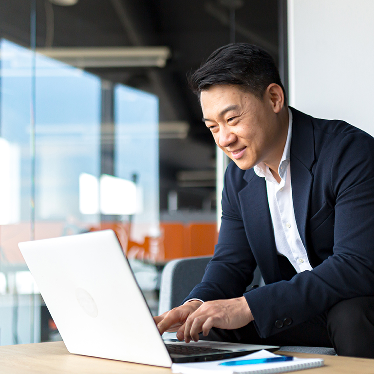 Senior Asian business man working on laptop online, smiling and rejoicing, happy boss business owner working in office