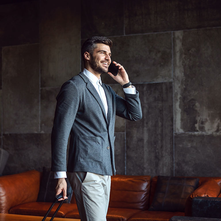 Good looking businessman walking in a hall of a hotel and having a phone call. He is carrying luggage. Business trip, technologies, telecommunications