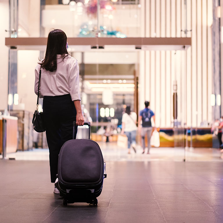 Asian young businesswoman walking and looking at the smartphone in hotel, woman in smart business casual carrying a suitcase - baggage in the hotel lobby area.