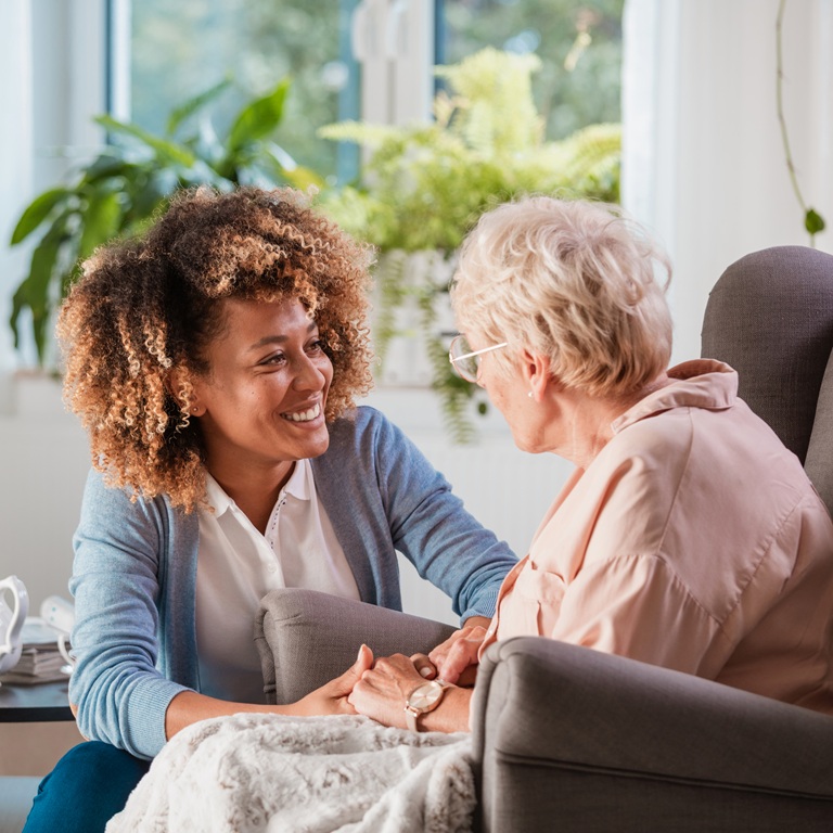 Caregiver talks with elderly woman in a sunny living room