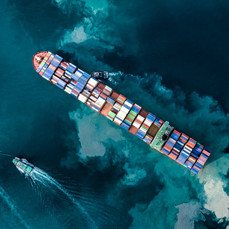 Cargo ship navigates water with support boats nearby