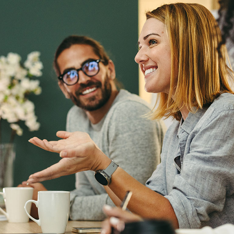 A team holds a discussion in a contemporary office, engaging with smiles and gestures. The atmosphere is lively, highlighting teamwork and communication among colleagues.