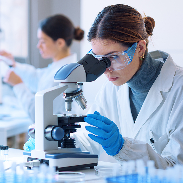 Young scientists conducting research investigations in a medical laboratory, a researcher in the foreground is using a microscope