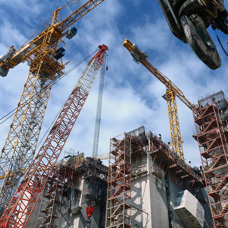 Close up of construction cranes and busy building site against blue sky