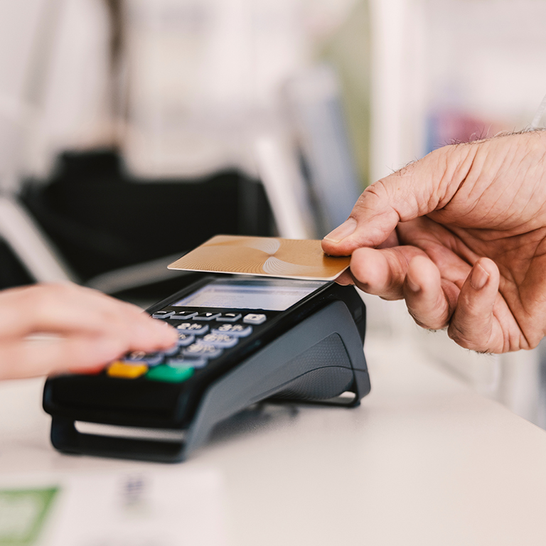 Close up of hand with credit card paying a bill at a point-of-sale (POS) terminal.