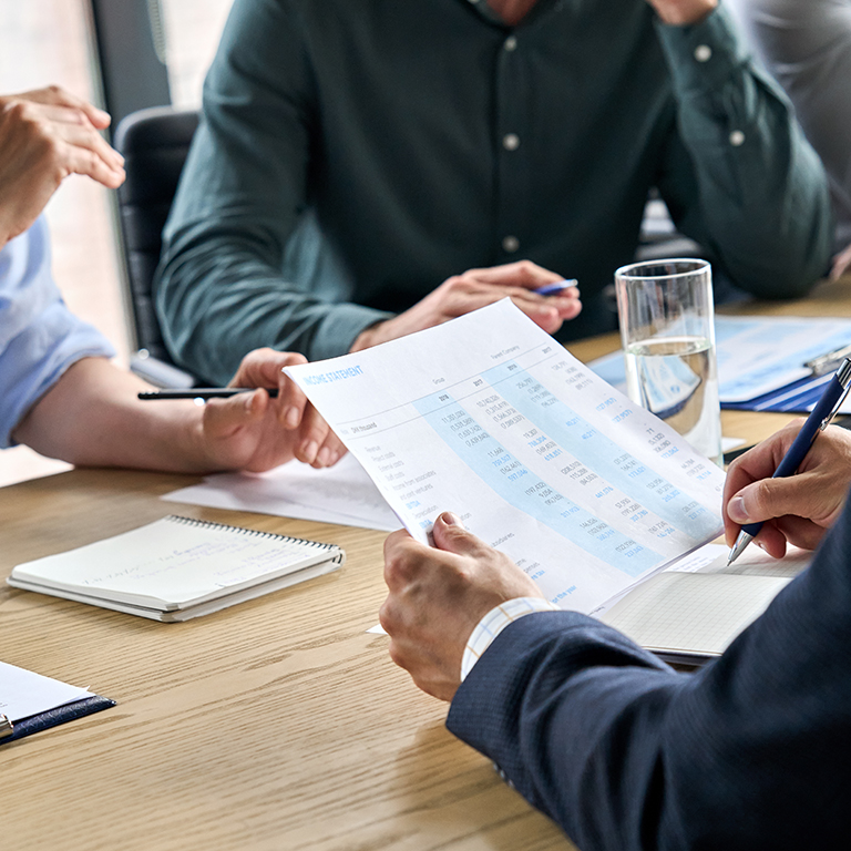 Closeup male hands making notes in corporation financial report. Businessman ceo executive manager and business team at table. Professional coworkers doing paperwork in office. Over shoulder view.