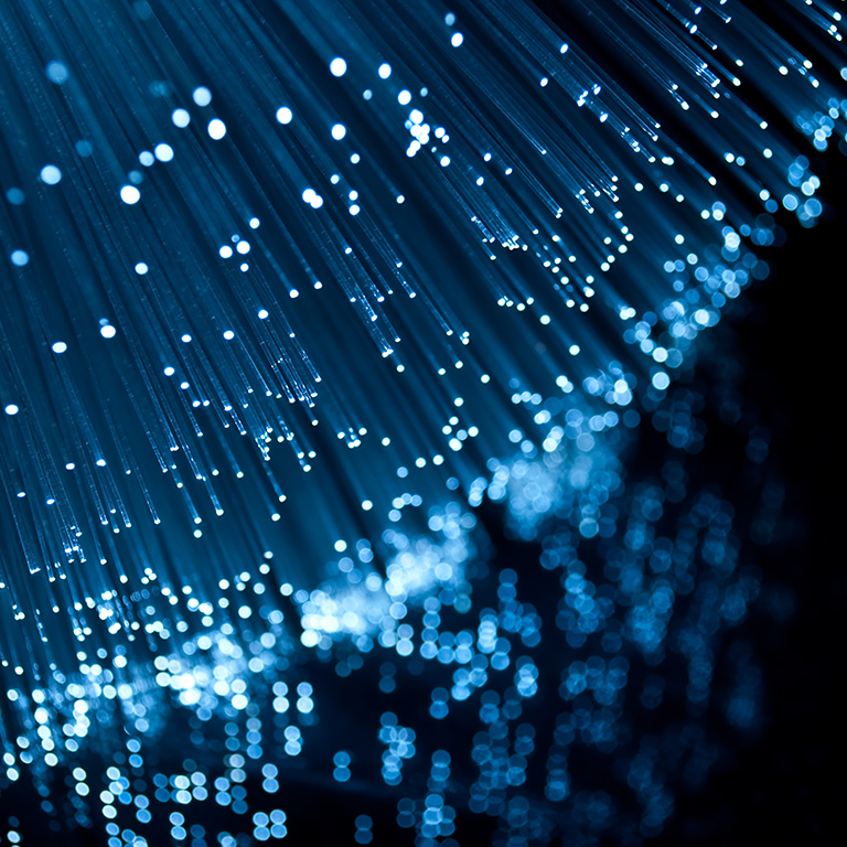 Close up on the ends of many blue illuminated fibre optic light strands against a black background and reflecting into the foreground.
