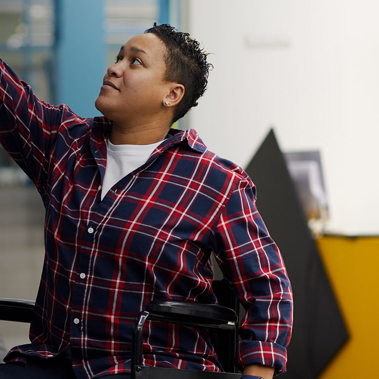 Portrait of disabled student in wheelchair choosing books while studying in college library, copy space